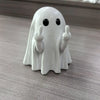 A white ghost figurine with black eyes and raised fingers, used for Halloween decor.