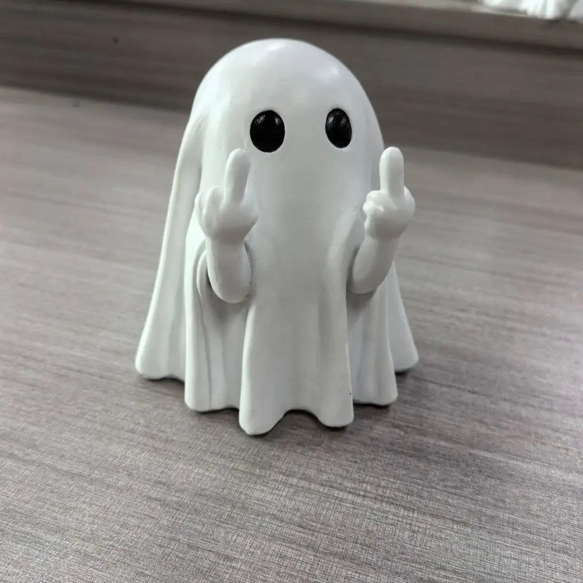 A white ghost figurine with black eyes and raised fingers, used for Halloween decor.