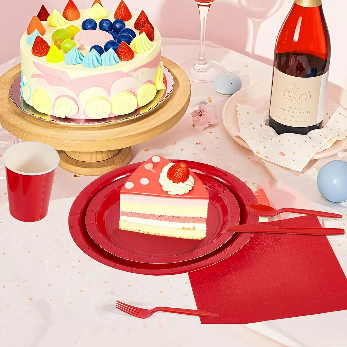 A red paper party tableware set featuring dinner plates, napkins, cups, and cutlery is displayed on a white tablecloth.