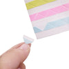 A hand is lifting a pink and yellow photo corner protector from a grid of colored plastic pieces.