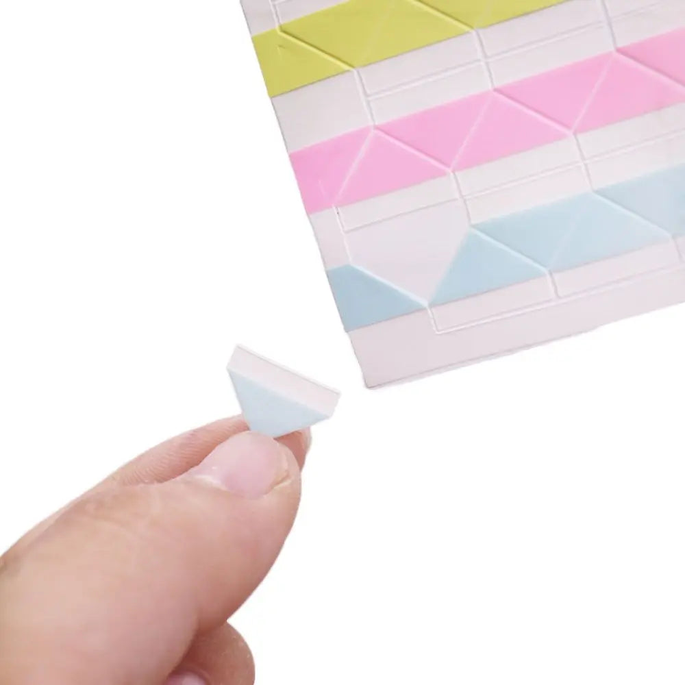 A hand is lifting a pink and yellow photo corner protector from a grid of colored plastic pieces.