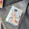 A clear plastic photo album with a card storage sleeve and a silver chain attached, resting on a gray fabric surface.