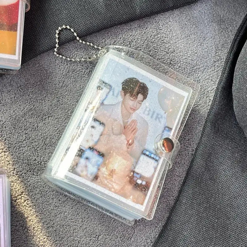 A clear plastic photo album with a card storage sleeve and a silver chain attached, resting on a gray fabric surface.