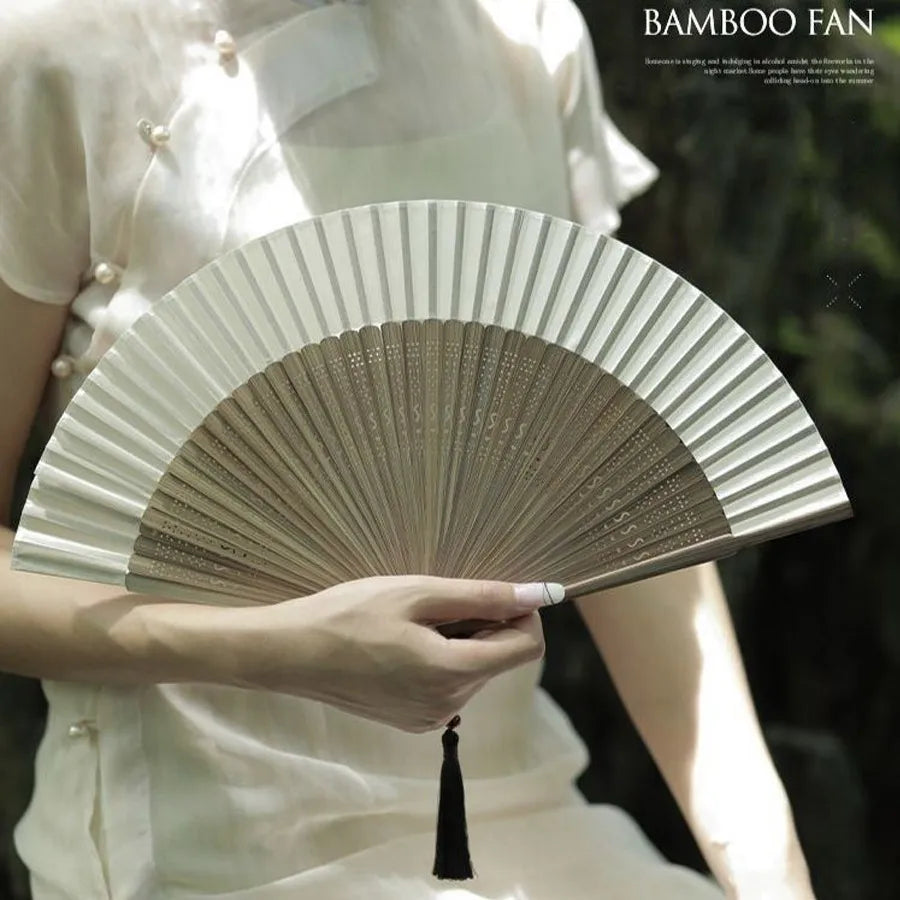 A person holds a classic bamboo folding fan with a decorative pendant against a natural background.