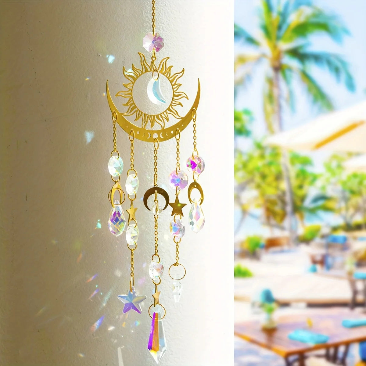 A golden sun and crescent moon wind chime with dangling crystal charms hanging on a white pillar.