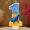 A birthday candle shaped like the number one, decorated with blue glitter and a small dinosaur figure.