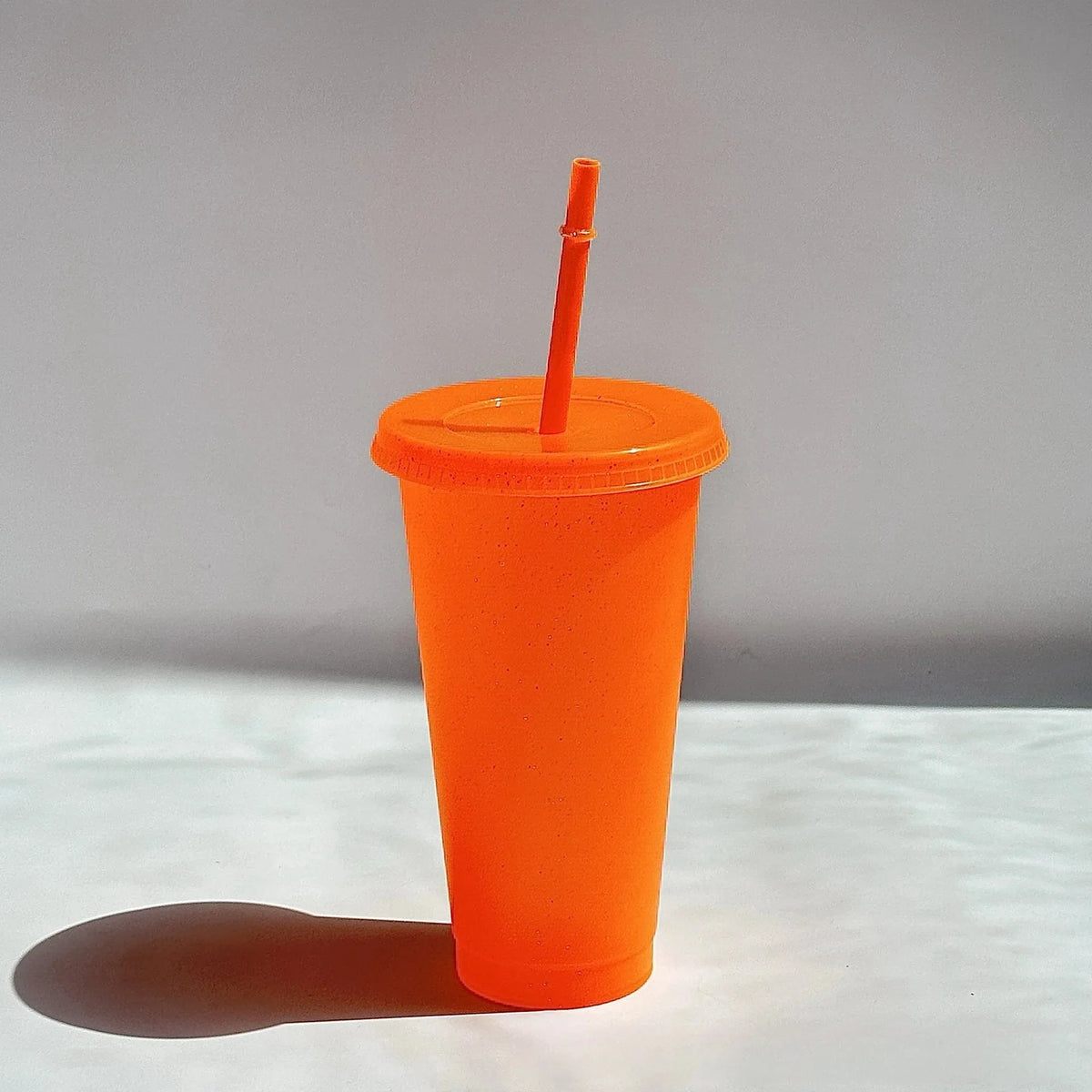 An orange plastic cup with a lid and a straw is shown against a light background.