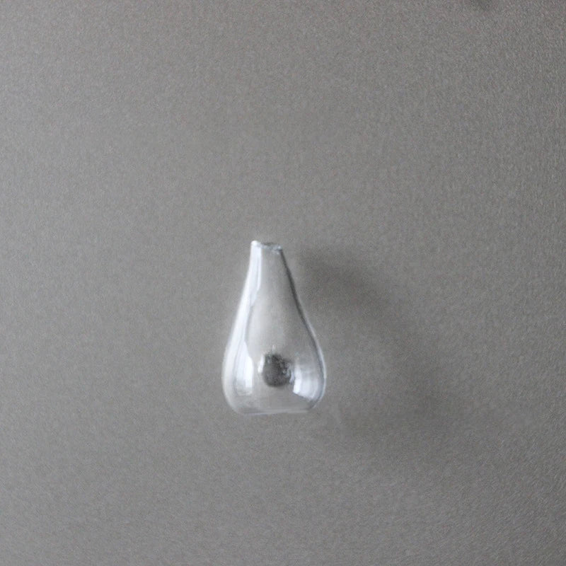 A clear glass fridge magnet shaped like a teardrop or inverted cone against a gray background.