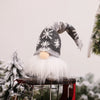 A white and gray knitted gnome decoration with a fluffy white beard and warm glow on a rustic stand.