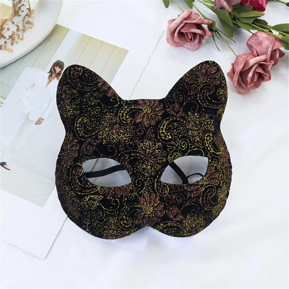 A black lace half-face mask with intricate gold and pink floral patterns is displayed on a white surface.