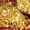 A pile of small, rectangular gold bars used for decor, scattered on a dark red surface.