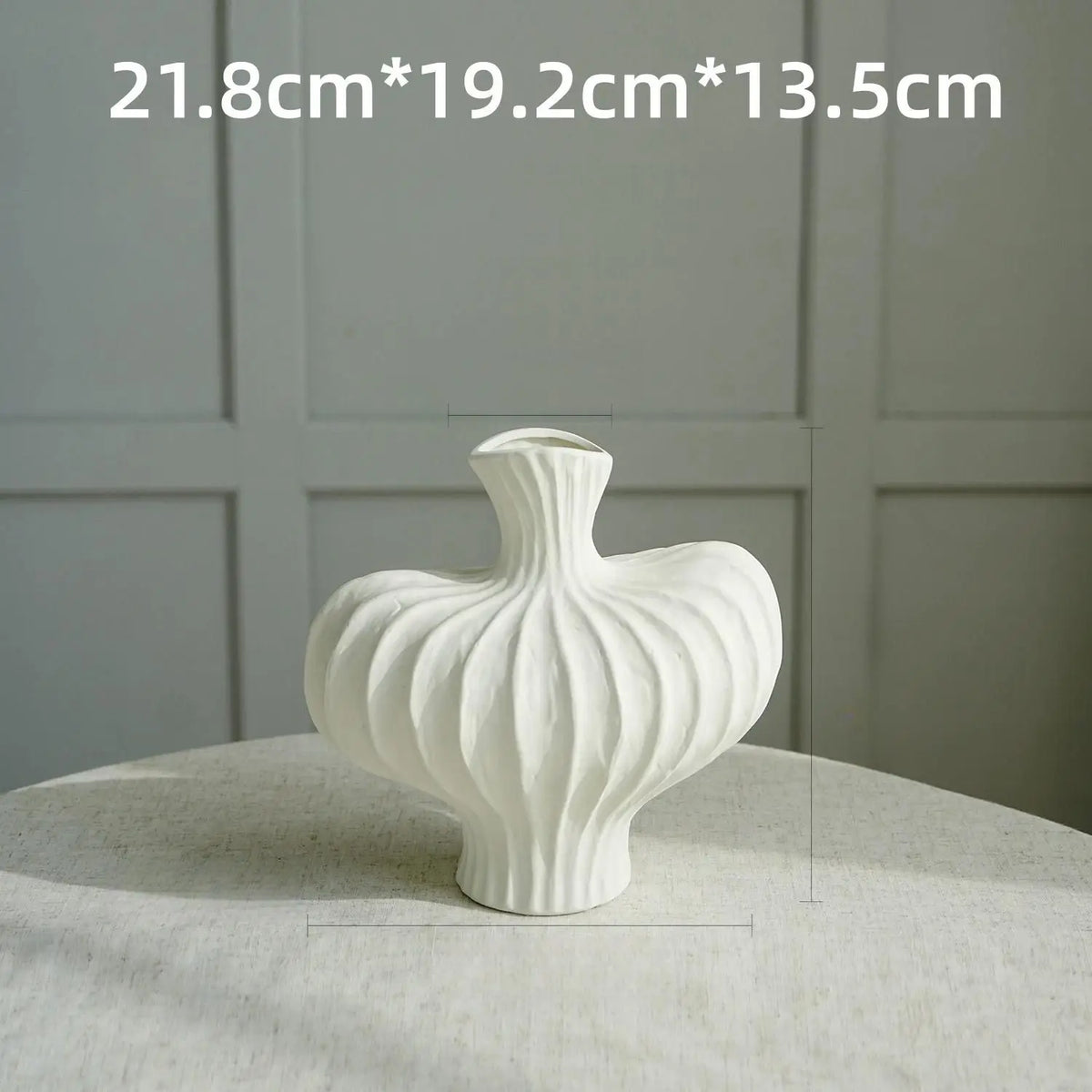 White ceramic vase with vertical fluting on a light surface.