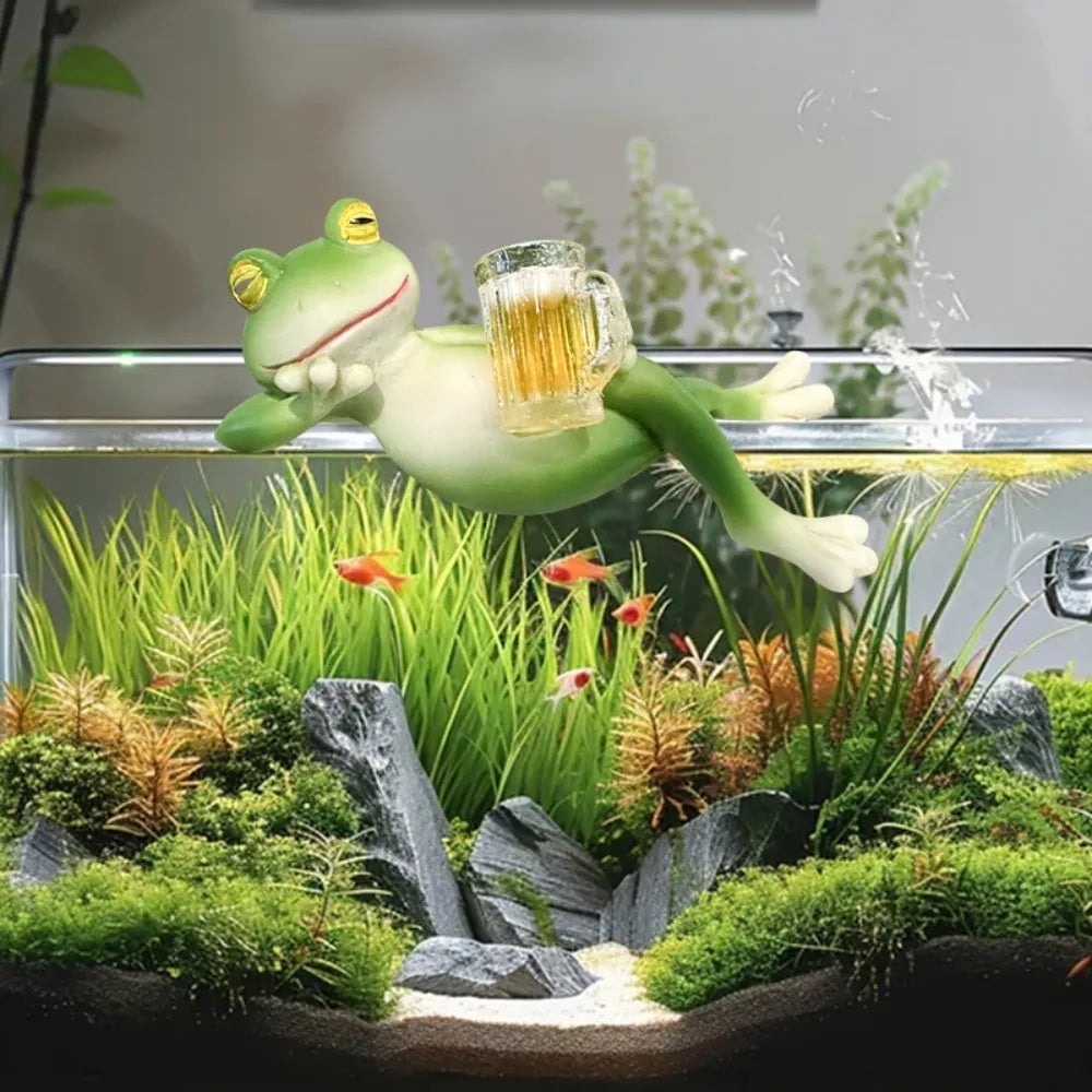 Una figura de rana de resina verde está posicionada sobre un vibrante paisaje acuático con plantas y rocas.