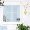 A light blue wooden louvered window frame decorated with small potted plants and a gold vase.