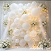 A large arrangement of matte white latex balloons decorated with white flowers and illuminated by string lights.
