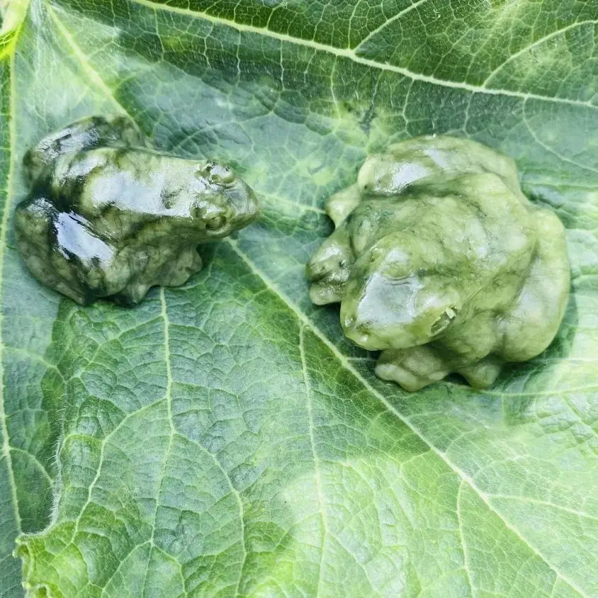 Statue de grenouille de jade verte, petite, posée sur une feuille verte éclatante.