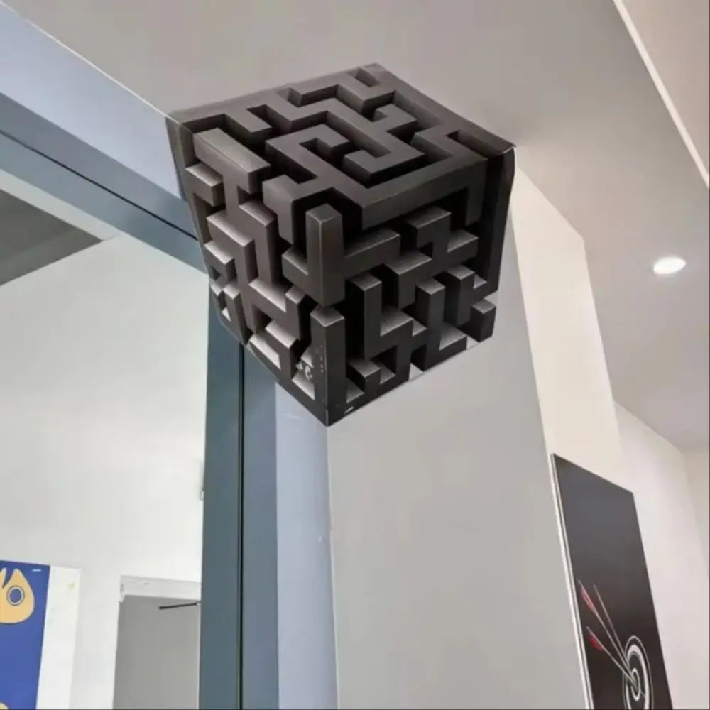 A black cube wall decal featuring an impossible maze pattern, mounted on a white wall.
