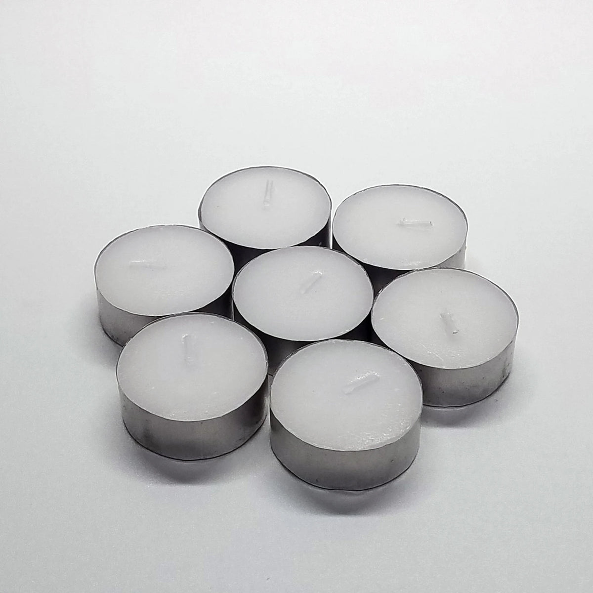 A cluster of six silver-colored tealight candles arranged on a white surface.