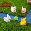 A set of mini white and pink farm animals including a pig, sheep, and a yellow animal placed in green artificial grass.