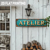 A vintage industrial metal wall sign with the word ATELIER in turquoise and golden distressed colors mounted on white wooden 