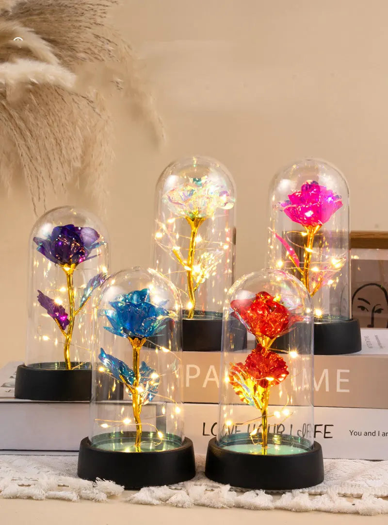 A glass dome featuring an eternal rose with a golden LED light displayed on a black base.