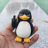 A black and white penguin desk statue with an angry expression and a raised flipper is held in a hand.