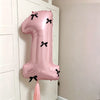 A large pink number balloon shaped like '1' with black bows, displayed next to a white cabinet.