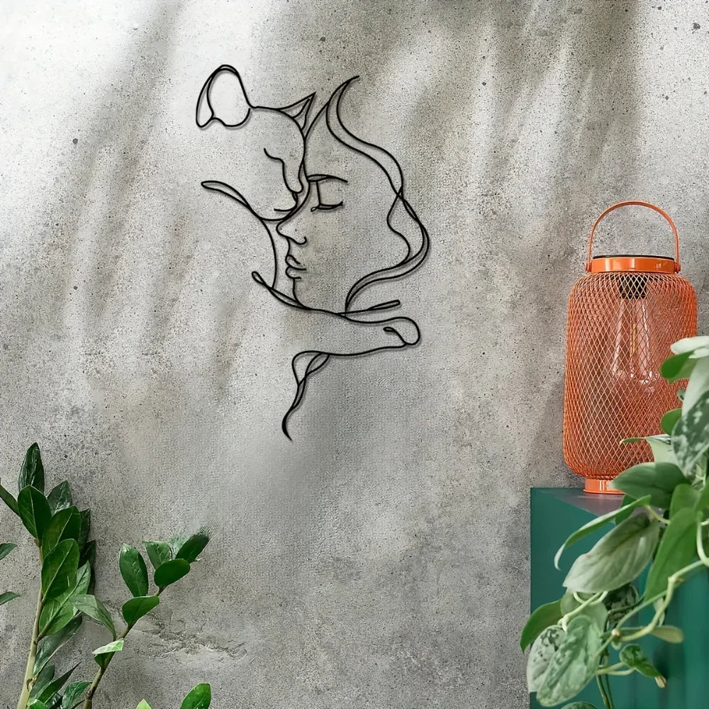 Black metal wall art silhouette of a woman and cat embracing on a gray concrete wall.