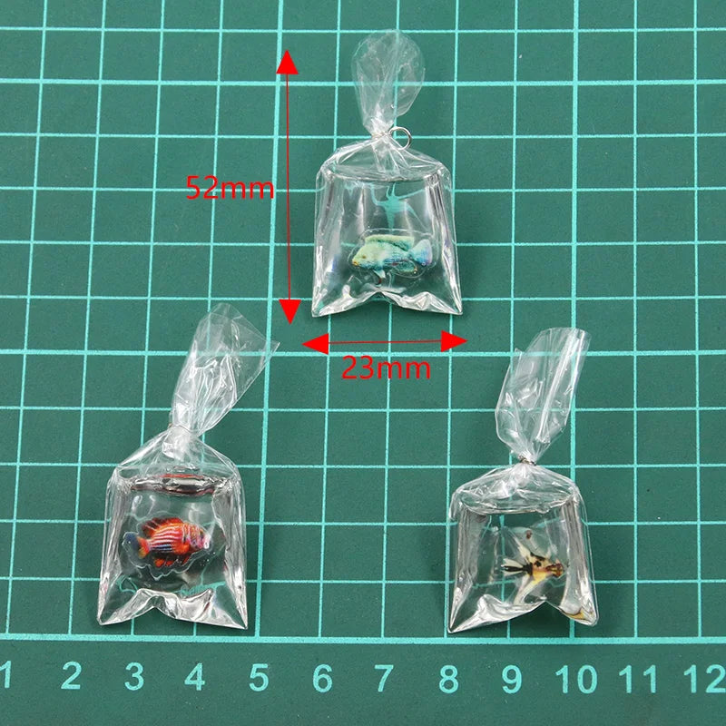 Tres bolsas de plástico transparente con pequeños collares de pez payaso de resina, dispuestos sobre un fondo de cuadrícula v