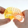 A hand holds a bright yellow and orange spring toy with numerous thin, black filaments.