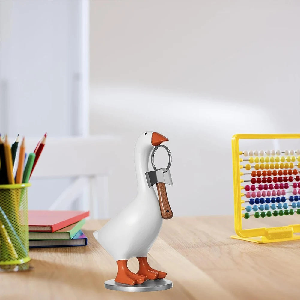 A white resin figurine of a goose with an attached key holder sits on a wooden surface next to a yellow magnetic rack.