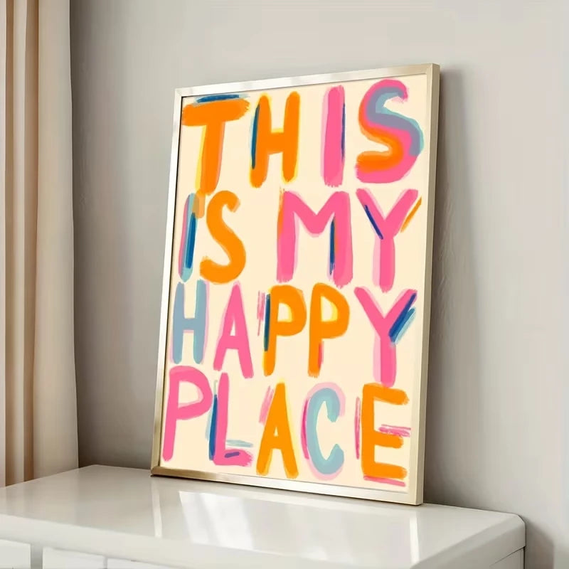 Impresión en lienzo enmarcada con texto colorido que dice "Este es mi lugar feliz", colgada en una estantería blanca.