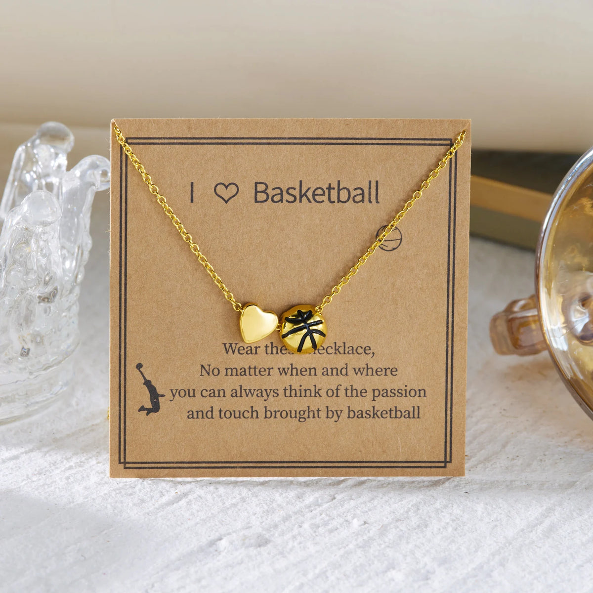 A gold heart-shaped basketball pendant necklace is displayed on a kraft paper card.