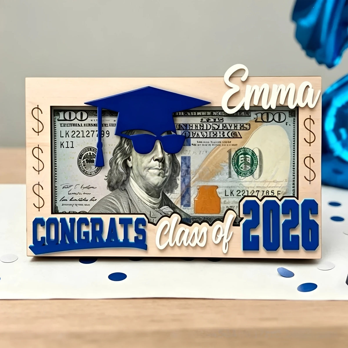A wooden sign featuring a graduation cap, sunglasses, and US currency, with the text Emma Congrats Class of 2026.
