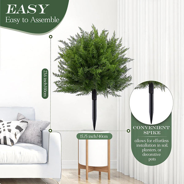 Artificial cedar ball tree with a black stake shown next to a white sofa.
