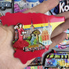 A red wooden fridge magnet shaped like Spain featuring a cityscape and landscape.