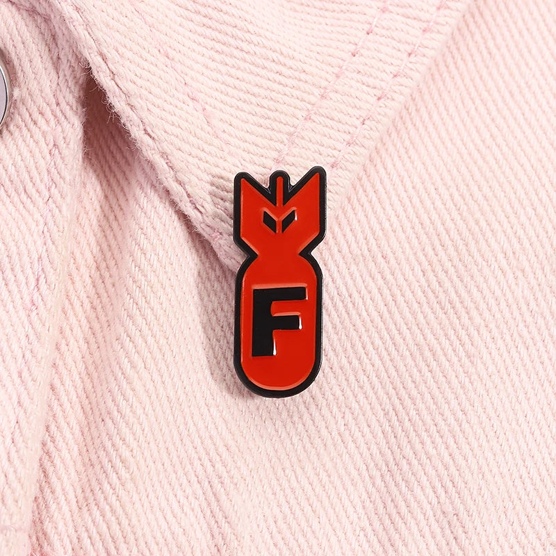 An enamel pin featuring a stylized red shark head design on a pink fabric collar.