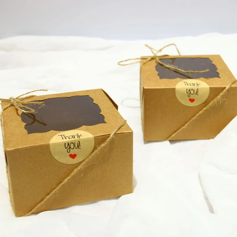 Two kraft paper favor boxes tied with twine and featuring a thank you heart sticker on a white surface.