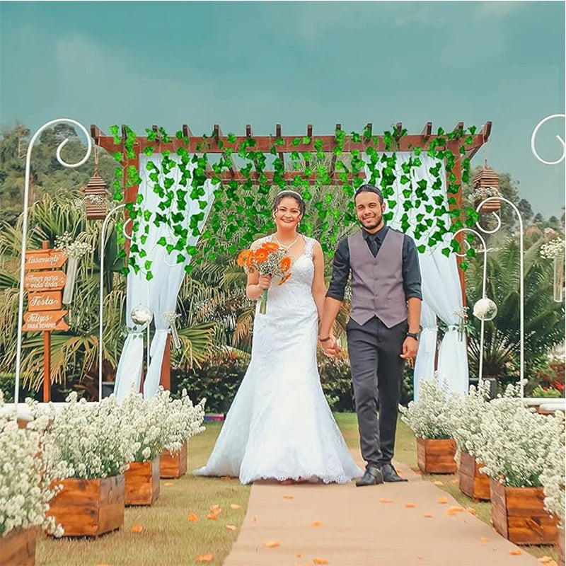 A bride and groom stand under a leafy archway decorated with artificial ivy vines for a wedding photo.