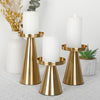 A set of three elegant gold metal candle holders with white pillar candles on a white surface.
