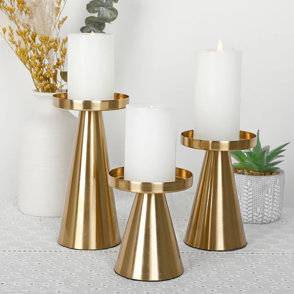 A set of three elegant gold metal candle holders with white pillar candles on a white surface.