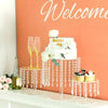A white wedding cake with 'Marry Me' inscription displayed on a clear acrylic stand with dangling crystals.