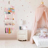 Wall-mounted headband holder display featuring colorful fabric headbands against a pink wall and crib