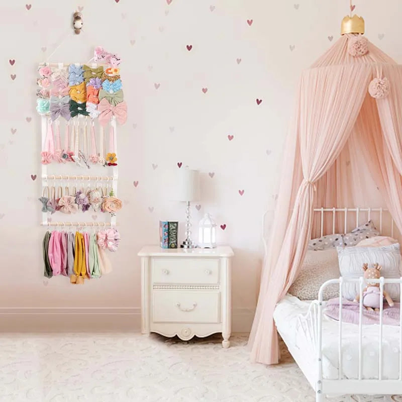 Wall-mounted headband holder display featuring colorful fabric headbands against a pink wall and crib