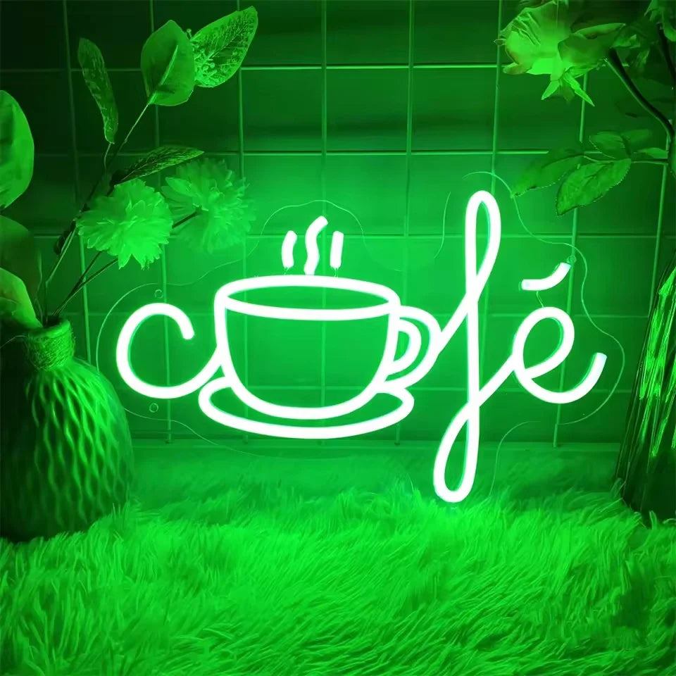 A neon sign shaped like a steaming cup of coffee and the word café glows bright green against a lush green background.