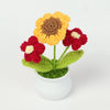 Hand woven crochet flowers in shades of orange and red growing in a white pot
