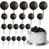 A set of twenty black ball cake toppers on sticks displayed above a silver cake.