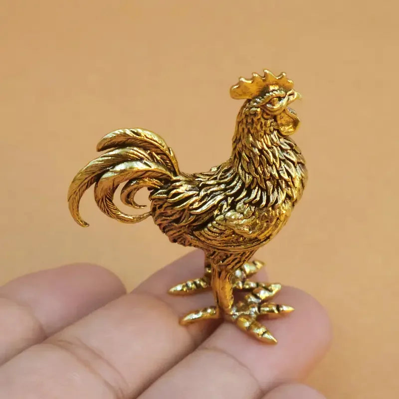 Handcrafted brass rooster figurine with intricate details resting on a hand.