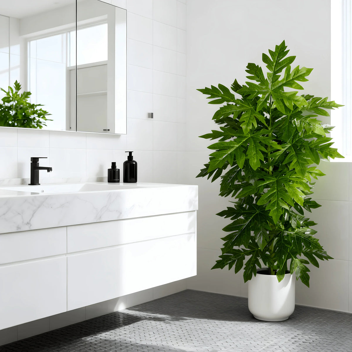 A large artificial papaya leaf plant in a white pot sits on a modern bathroom counter next to a sink.