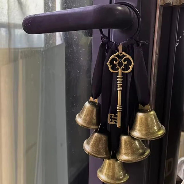 A vintage bronze witch door handle keywind chime set with a decorative key and multiple brass bells hanging from a dark purpl